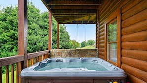 A wooden cabin with a hot tub on a deck, surrounded by greenery. - Spacious Family Fun Cabin with Slide, Hot Tub, Games & Great Location! Pets ok (Pigeon Forge)