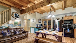 A spacious living room with a wooden ceiling, a brown leather sofa, a wooden dining table with benches, and a kitchen area with modern appliances. - Spacious Family Fun Cabin with Slide, Hot Tub, Games & Great Location! Pets ok (Pigeon Forge)