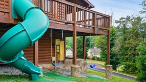 A wooden cabin with a green slide and swings. - Spacious Family Fun Cabin with Slide, Hot Tub, Games & Great Location! Pets ok (Pigeon Forge)