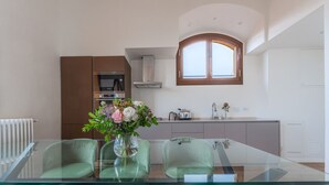 Une cuisine moderne avec une table à manger en verre, des chaises vertes et un vase de fleurs.