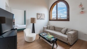 Un salon moderne comprenant un canapé, un fauteuil, une table basse, un téléviseur et une grande fenêtre donnant sur un beau paysage.