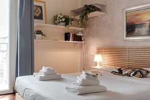 A hotel room with a bed, a bedside table with a lamp, a wall-mounted shelf with books and a plant, and a painting on the wall. - Le Margherite - Sweet Dreams in Florence (Firenze)