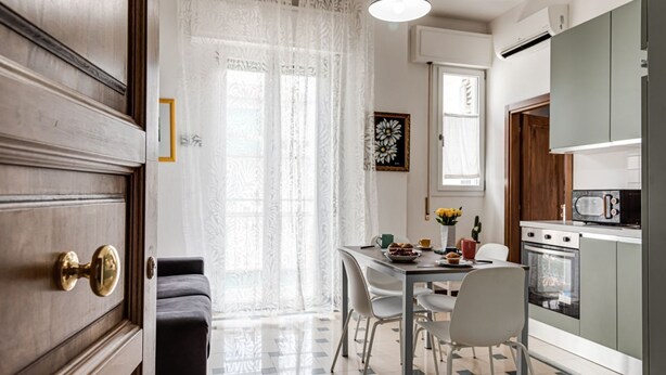 A kitchen with a stove, oven, and microwave. There is a dining table with chairs and a window with curtains. - Le Margherite - Sweet Dreams in Florence (Firenze)