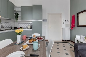 A modern kitchen with grey cabinets, a white countertop, and a dining area with a table set for breakfast. - Le Margherite - Sweet Dreams in Florence (Firenze)
