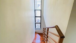 A staircase with wooden steps and a metal railing, leading to a room with a large window and a decorative light fixture. - Townhouse with a pool, arcade/gaming area and a massage chair! (City of Naga)