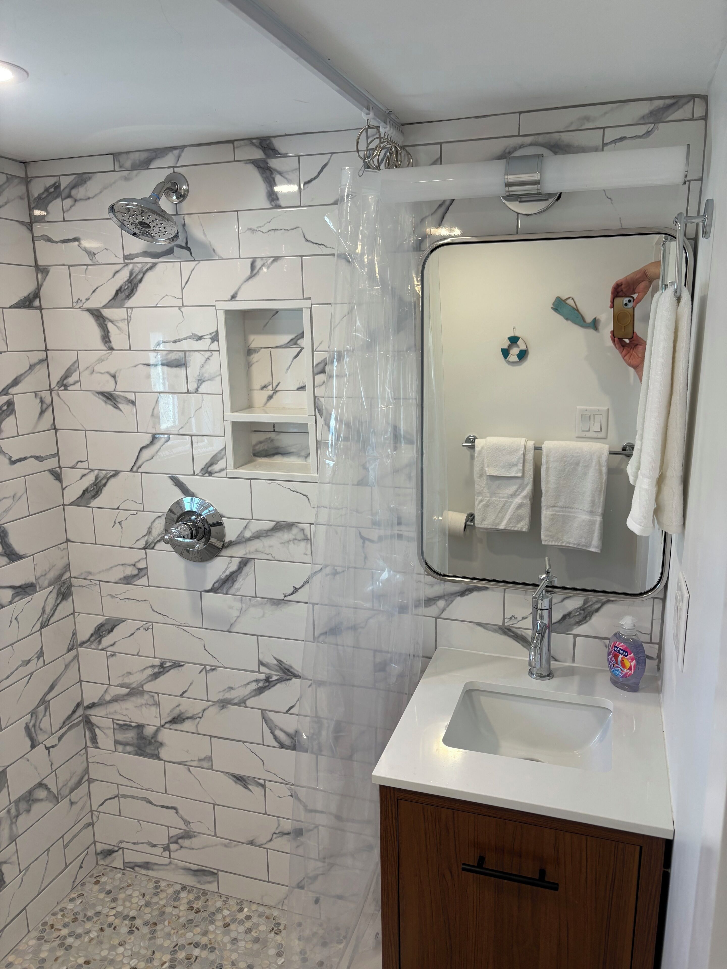 Ein Badezimmer mit Marmorfliesen, einer Dusche, einem Waschbecken inklusive Spiegel und einem Holzkabinent.