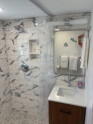 Ein Badezimmer mit Marmorfliesen, einer Dusche, einem Waschbecken inklusive Spiegel und einem Holzkabinent.