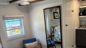 A bedroom with a bed, a chair, a window with a view, a mirror, and a kitchenette. - Enjoy easy beach access and awesome bay views as soon as you step out the studio (Provincetown)
