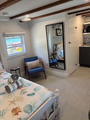 Une chambre avec un lit, une chaise, une fenêtre donnant sur un beau paysage, un miroir et un coin cuisine.