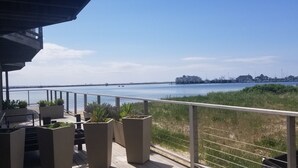 A balcony with a view of the sea, a ship, and a distant cityscape. - Enjoy easy beach access and awesome bay views as soon as you step out the studio (Provincetown)