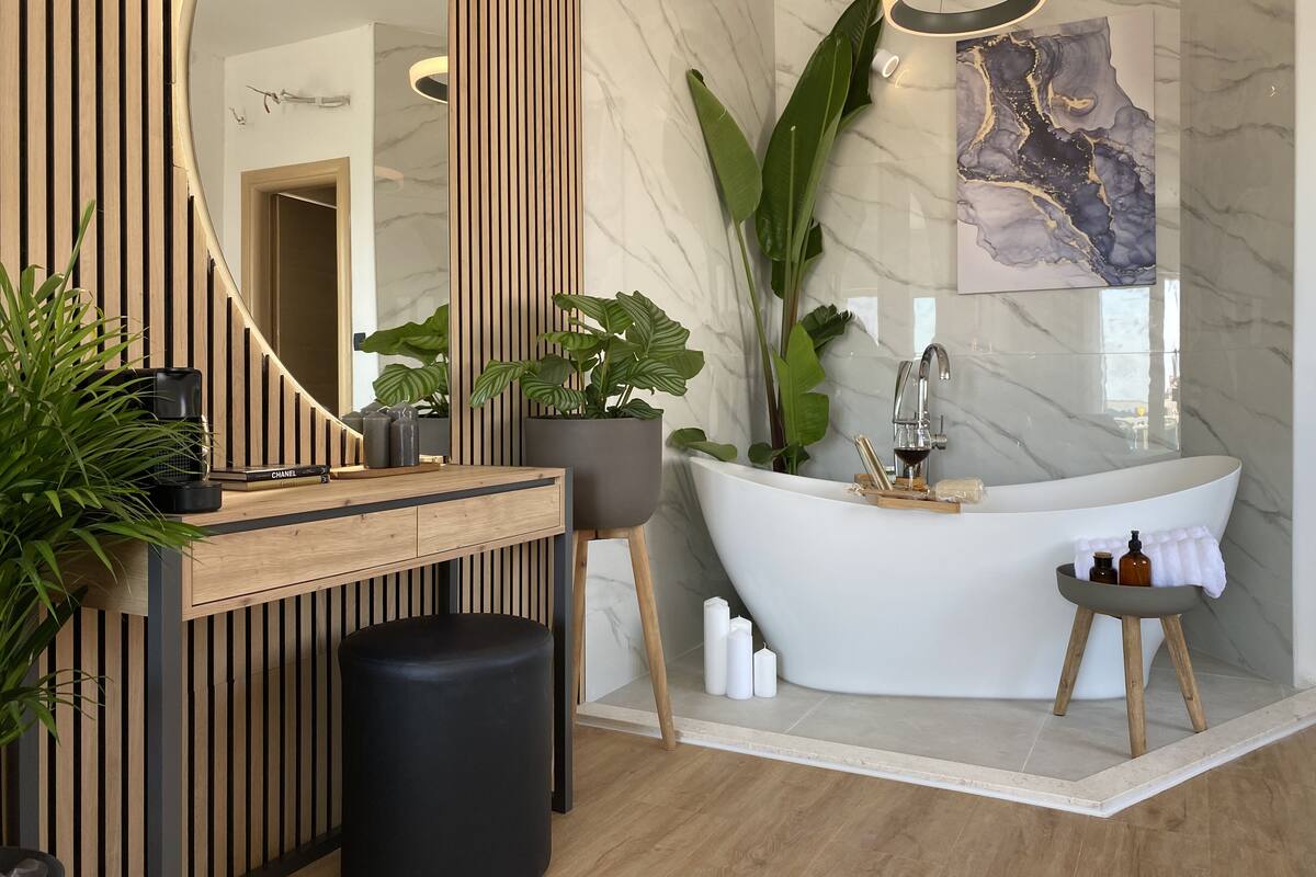 Un baño moderno con una bañera independiente, un espejo grande y una pared de mármol.