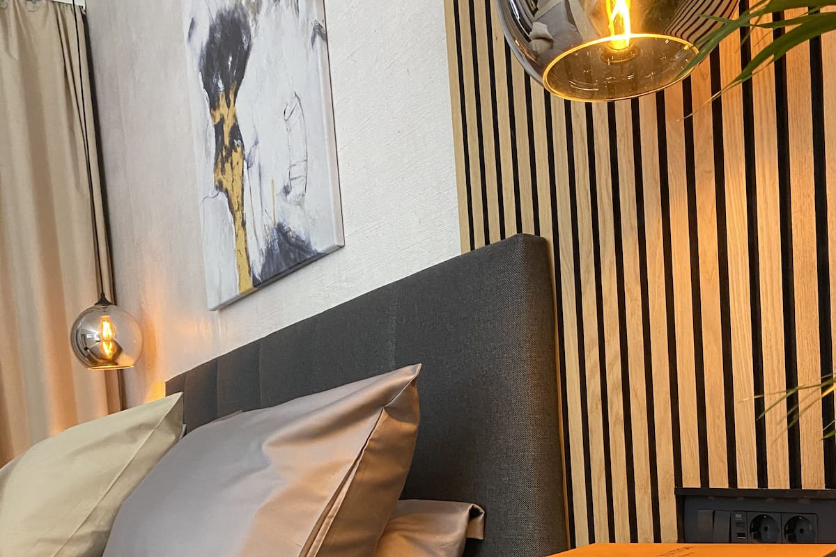 Un dormitorio moderno con cama, almohadas, una estantería de pared y un cuadro.