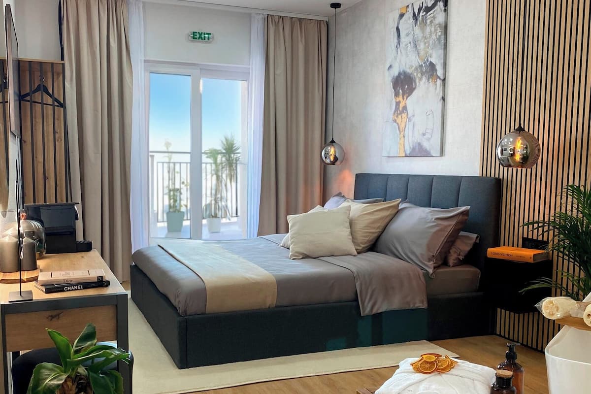 Habitación de hotel moderna con una cama grande, un escritorio con una computadora portátil, una planta en maceta y vistas al exterior.