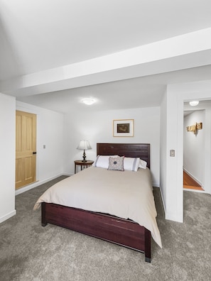 A bedroom with a large bed, a wooden door, a nightstand with a lamp, and a framed picture on the wall. - Charming 2 Bedroom Apartment Downtown In Vibrant Bozeman (Bozeman)