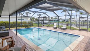 A covered swimming pool with lounge chairs and a view of palm trees and houses in the background. - Waterfront Oasis, Pool, Dock, Location! (Cape Coral)