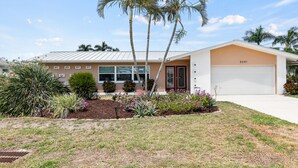 A two-story house with a garage, palm trees, and a well-maintained lawn. - Waterfront Oasis, Pool, Dock, Location! (Cape Coral)