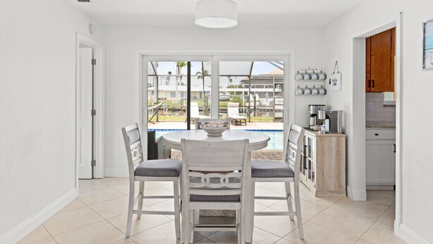A modern kitchen with white cabinets, a dining area with a round table and chairs, and a view of a swimming pool. - Waterfront Oasis, Pool, Dock, Location! (Cape Coral)