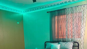 Quarto com cama, mesa de cabeceira, ventoinha no teto e janela com cortinas estampadas.