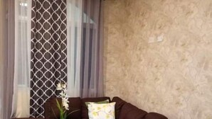 Ein Wohnzimmer mit braunem Sofa, einem Glastisch mit Pflanzen und einem gemusterten Vorhang.