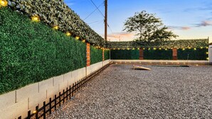 Un patio con suelo de grava, un banco de madera, un muro de ladrillo y un seto.