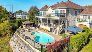 Una casa grande con piscina, mobiliario exterior y un patio cubierto.