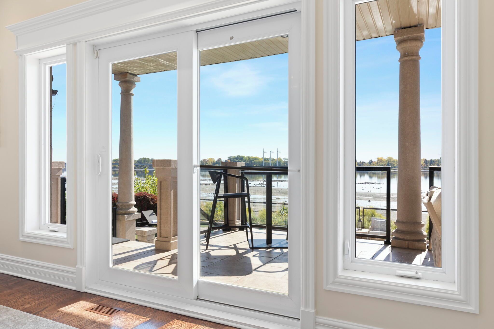 A room with a sliding glass door leading to an outdoor patio with a view of a body of water and a distant shoreline.