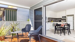 Une cuisine moderne avec des meubles blancs, un coin repas avec deux chaises et une porte-fenêtre coulissante donnant sur une terrasse avec une table et des chaises.