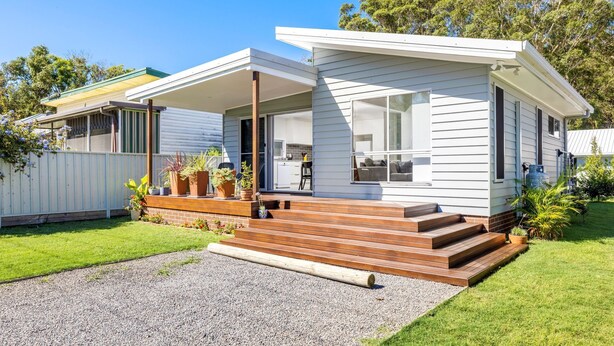 Une maison moderne de plain-pied dotée d’un porche couvert, d’une petite terrasse et d’une allée gravillonnée.