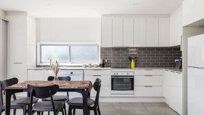 Une cuisine moderne avec des meubles blancs, une table à manger avec des chaises, une machine à café et un mur de fond en briques.