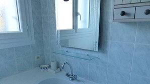 Une salle de bain avec un lavabo blanc, un miroir et une fenêtre.