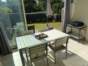 Een terras met een tafel, stoelen, een barbecue en een schuifpui naar een tuin.