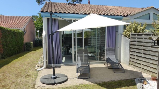 Une terrasse avec un parasol blanc, deux chaises longues et une porte vitrée donnant sur un espace intérieur.