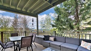 A covered outdoor deck with a table and chairs, a sofa, and a glass-top coffee table. - Chalumeau - RVMT (Mont-Tremblant)
