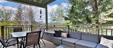 A covered outdoor deck with a table and chairs, a sofa, and a glass-top coffee table.