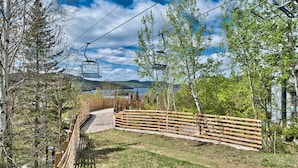 A wooden bridge leading to a ski lift with a view of a lake and hills in the background. - Chalumeau - RVMT (Mont-Tremblant)