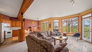 A spacious living room with a large sofa, a dining table, and a kitchen area with wooden cabinets and a white refrigerator. - Chalumeau - RVMT (Mont-Tremblant)