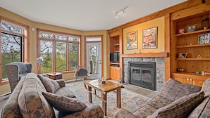 A cozy living room with a fireplace, large windows, and a wooden bookshelf. - Chalumeau - RVMT (Mont-Tremblant)