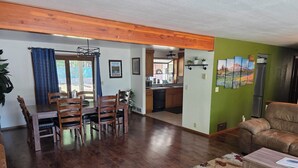 A spacious living area with a wooden dining table and chairs, a sofa, and a coffee table. A kitchen is visible in the background.
