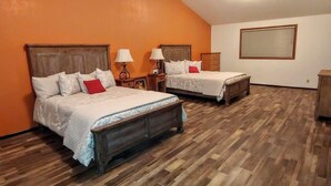 A room with two beds, wooden flooring, and orange walls.