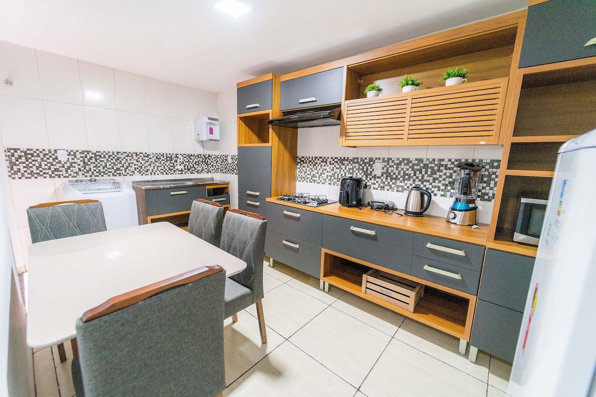 Una cocina moderna con armarios grises y de madera, una mesa de comedor con sillas y un microondas.
