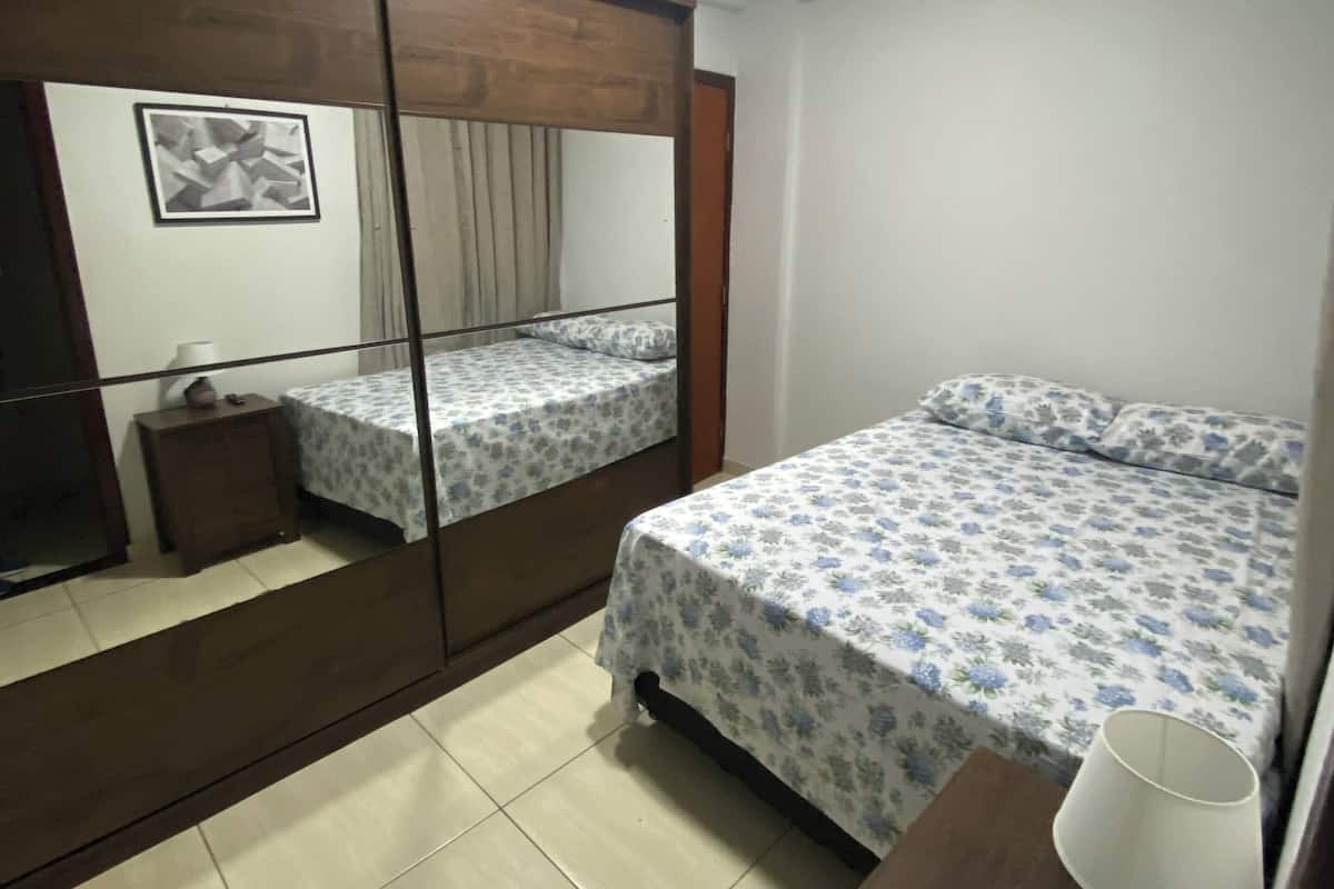 Un dormitorio con una cama, una mesita de noche, un espejo y una lámpara en el techo.
