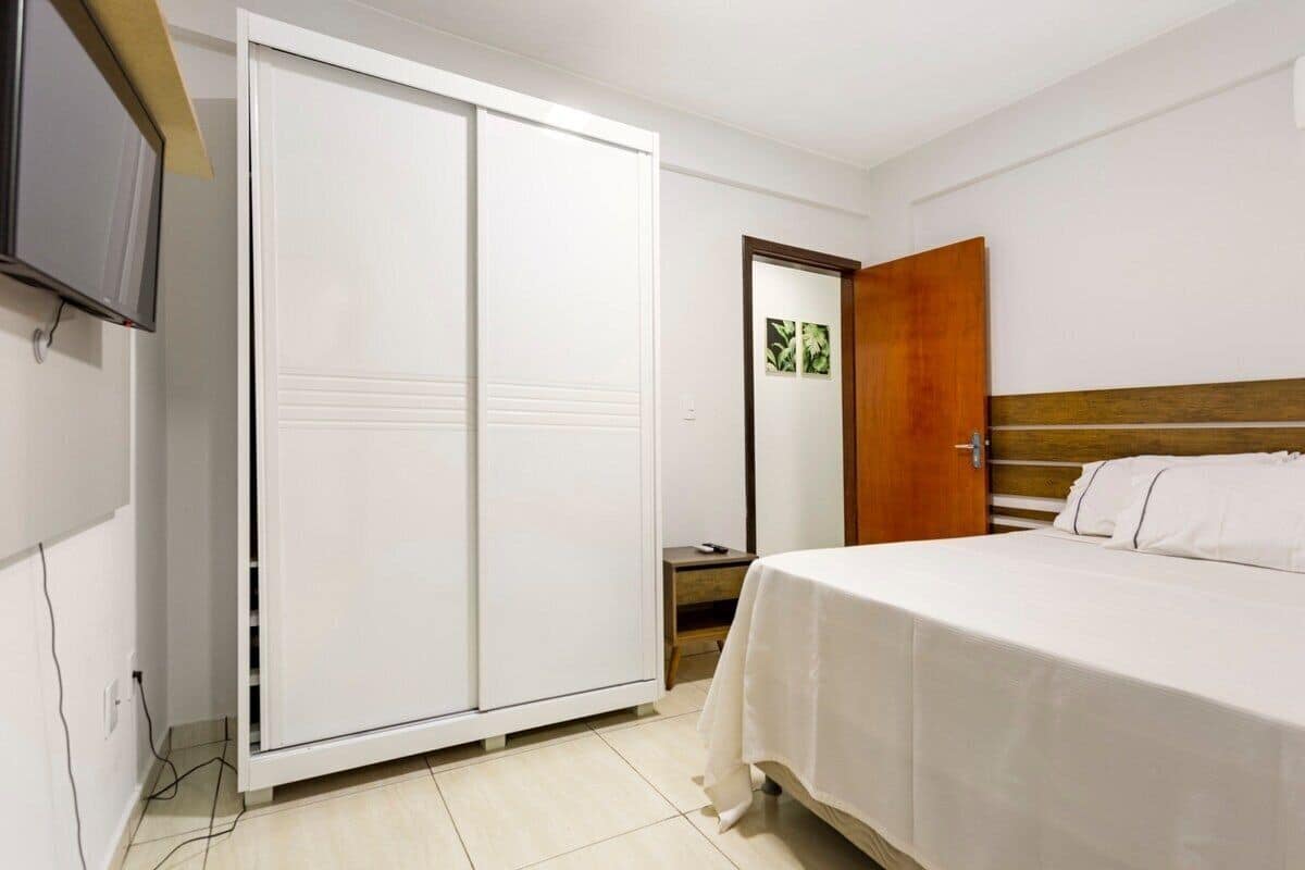 Un dormitorio con una cama, un armario, un televisor y una puerta que da a otra habitación.