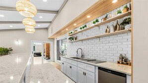A modern kitchen with white brick backsplash, wooden shelves with plants, and a built-in dishwasher. - Blue Skies Retreat - Custom-Built Retreat in the Suburbs! (Farmington Hills)