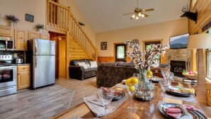 A cozy living room with a wooden staircase, a fireplace, and a dining area set with a table and chairs.