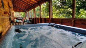 A hot tub in a wooden cabin with a view of trees.