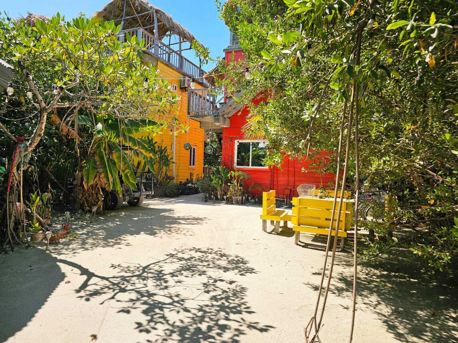 A courtyard with a yellow bench, a red building, and a thatched-roof structure.