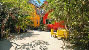 A courtyard with a yellow bench, a red building, and a thatched-roof structure.
