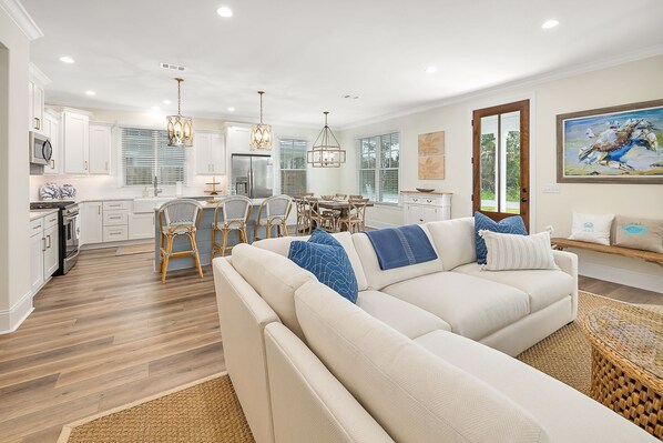 A modern kitchen with white cabinets, a dining area with wicker chairs, and a living room with a beige sofa and decorative pillows. - Private Heated Pool, Close to Beaches, Restaurants & Shopping! (Saint Simons Island)