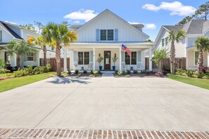 A two-story house with a front porch, a flag, and a well-maintained lawn. - Private Heated Pool, Close to Beaches, Restaurants & Shopping! (Saint Simons Island)