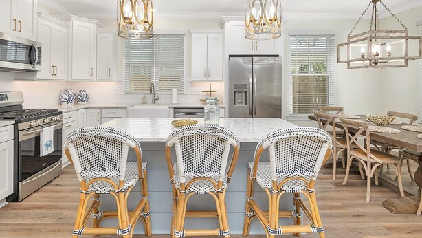 Een moderne keuken met witte kastjes, een roestvrijstalen koelkast en een centraal eiland met rieten stoelen.